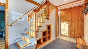 Una escalera de madera con estantes empotrados y un banco, que conduce a una habitación con una puerta grande de madera y un zapatero.