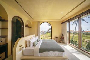 A bedroom with a large bed, a nightstand, a lamp, and a view of a landscape through a window. - Didi Apartment Seseh (Munggu)