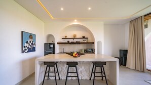 Uma cozinha moderna com ilha central, banquetas, micro-ondas e geladeira.