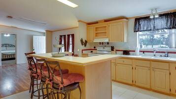 A kitchen with wooden cabinets, a central island with bar stools, a stove, and a window with curtains.