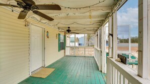 Une véranda avec un plancher en bois peint en vert, des balustrades blanches et un ventilateur de plafond.