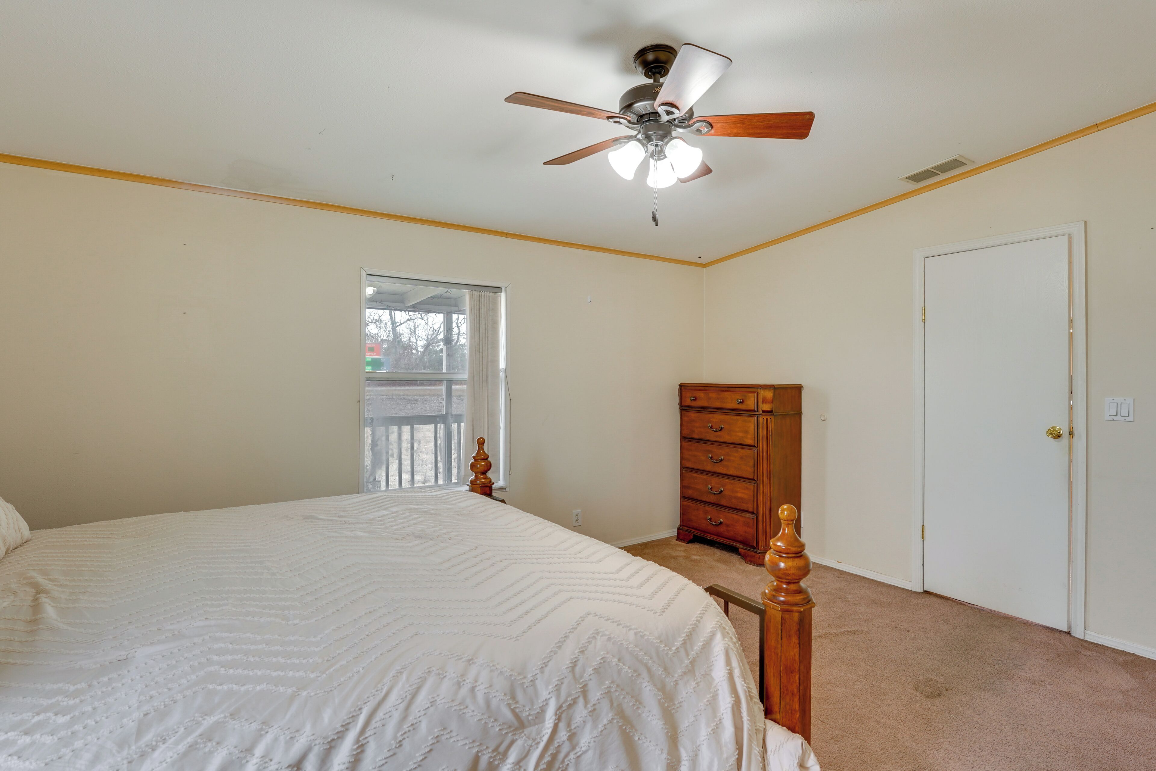 A bedroom with a bed, a dresser, a door, and a ceiling fan.