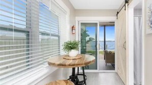 A narrow balcony with a wooden table and two stools, a potted plant, and a view of the sea through a glass door. - Bayfront Condo, Prime Beach Access, Manasota Key (Englewood)