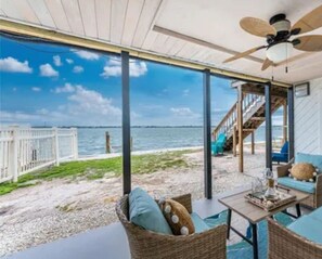 A covered outdoor seating area with wicker furniture, a ceiling fan, and a view of the beach and ocean.