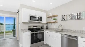 A modern kitchen with white cabinets, stainless steel appliances, and a view to the outside. - Bayfront Condo, Prime Beach Access, Manasota Key (Englewood)
