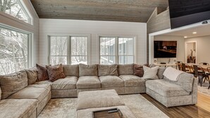 Ein großes, L-förmiges Sofa mit mehreren Kissen, einem Holztisch und einem flachbildfernseher an der Wand.