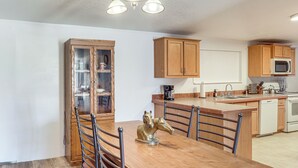 A kitchen with wooden cabinets, a microwave, a sink, and a dining area with a table and chairs. - Magnolia Manor House: Desert Escape, Mtn Views (Dolan Springs)