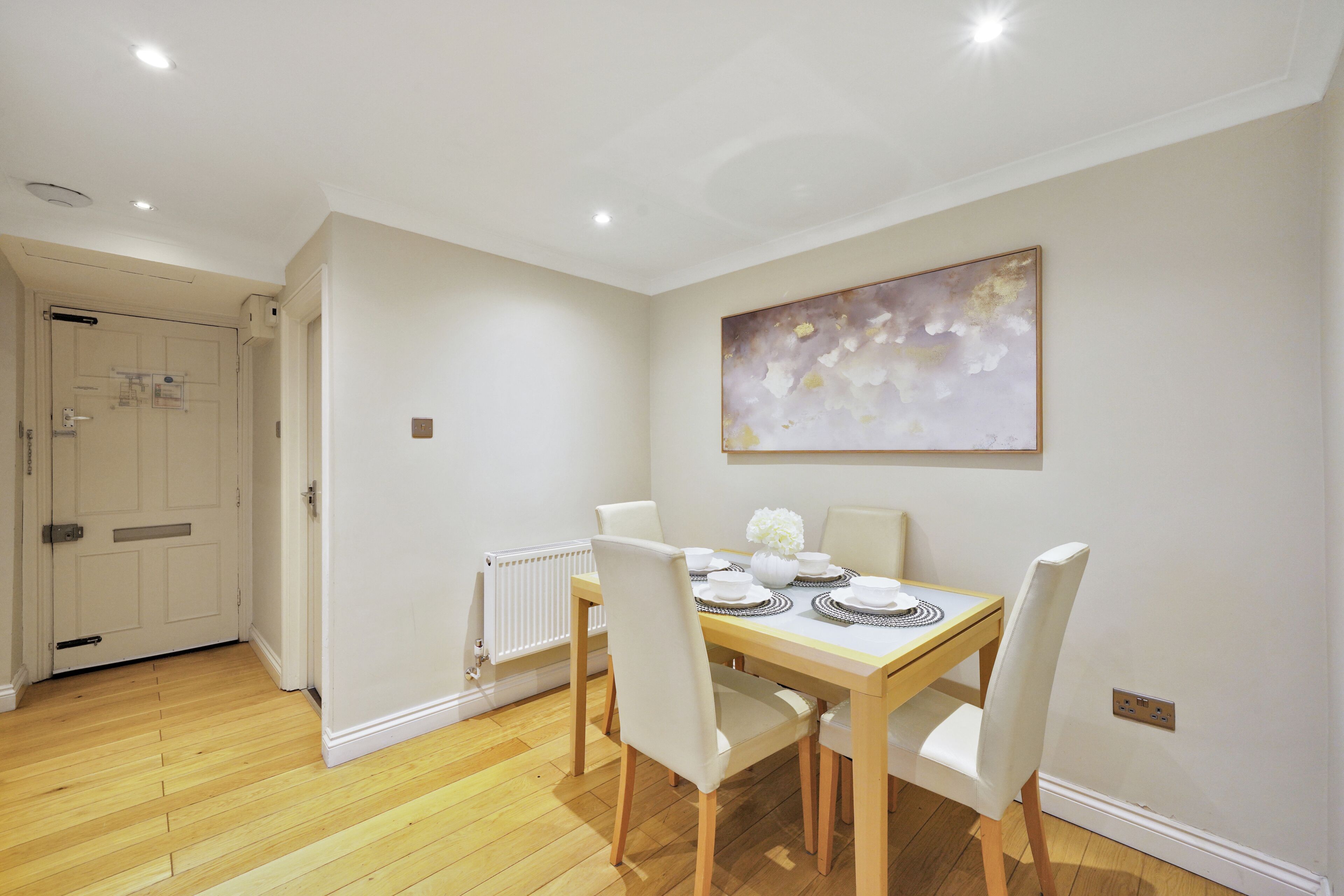 Un coin repas avec une table en bois, des chaises blanches et un tableau abstrait accroché au mur.