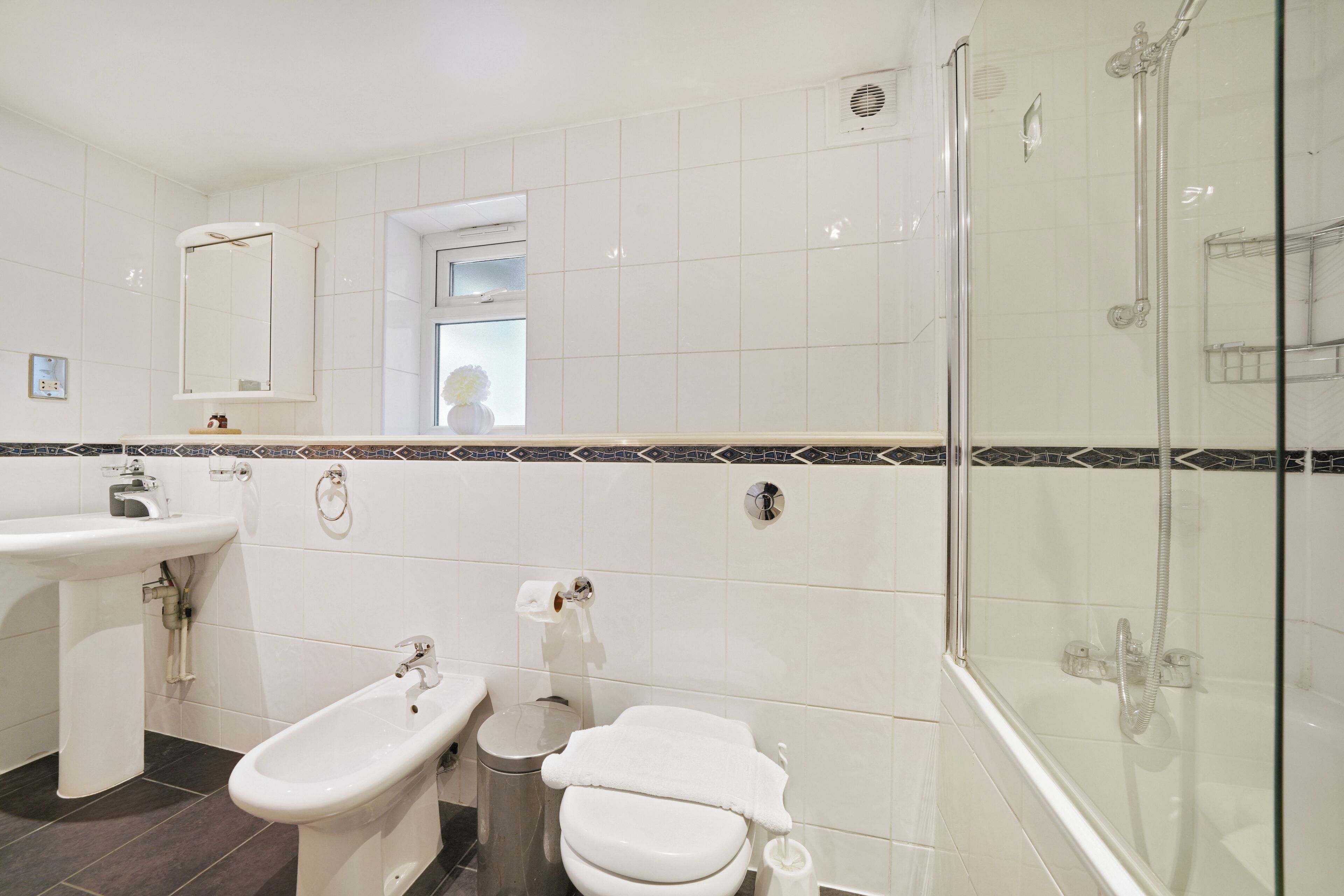 A bathroom with a bidet, toilet, sink, and glass-enclosed shower.