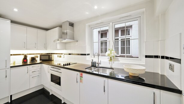 A modern kitchen with white cabinetry, a black countertop, a stainless steel range hood, a microwave, and a sink. - Hertford Flat 2 (London)