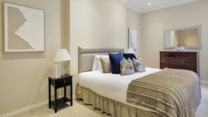 A bedroom with a bed, bedside table, dresser, and a large abstract painting on the wall. - Hertford Flat 2 (London)
