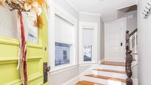 Una scala con gradini in legno che conduce a una porta bianca, una porta verde con un asciugamano rosso appeso, e una finestra con vista su un edificio.