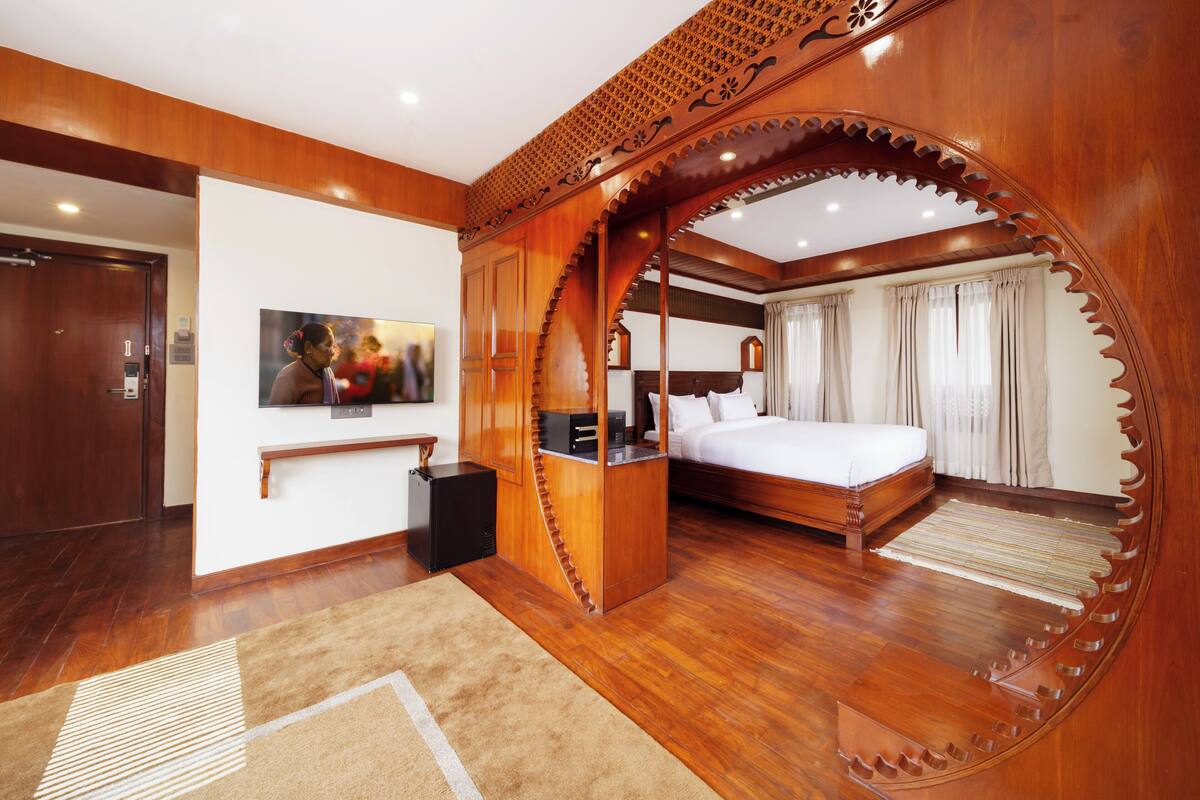 A hotel room with a wooden floor, a bed, a TV, a desk, and a wardrobe.