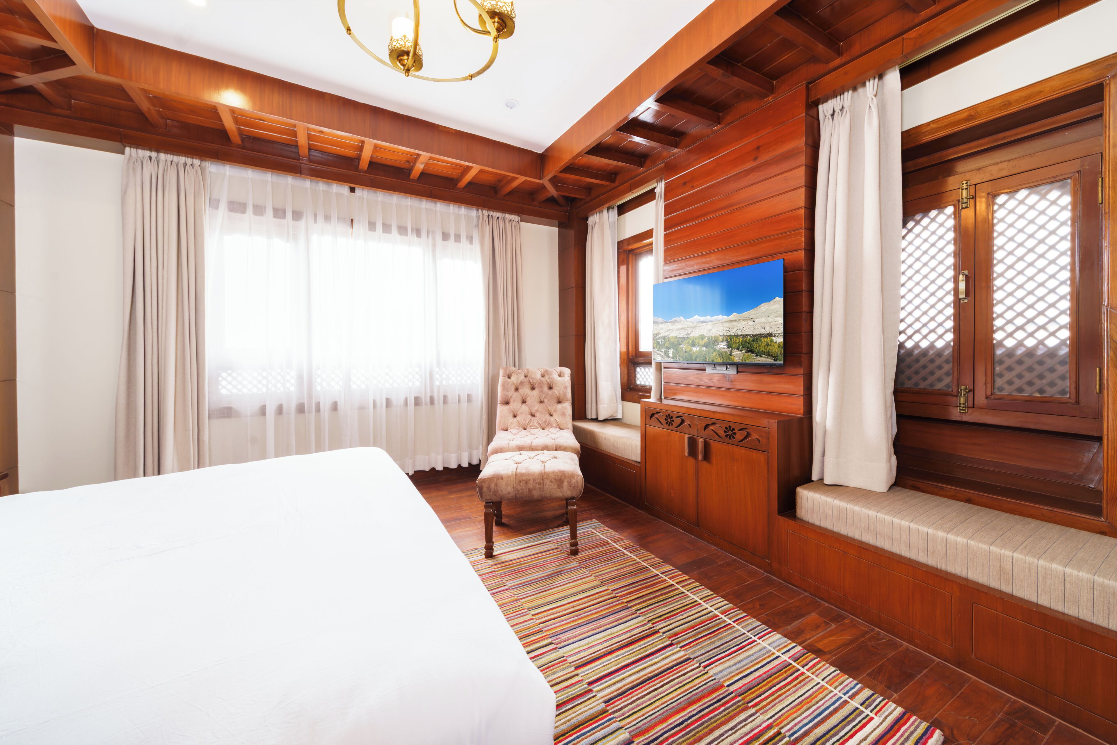 Una habitación de hotel con una cama, un sillón tapizado, un televisor y una ventana con cortinas.