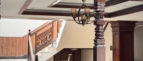 A wooden staircase with intricate carvings, a chandelier, and a view of the upper floor.