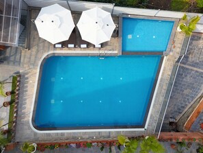 Une piscine rectangulaire avec une terrasse carrelée, deux parasols blancs et des plantes en pot disposées tout autour.