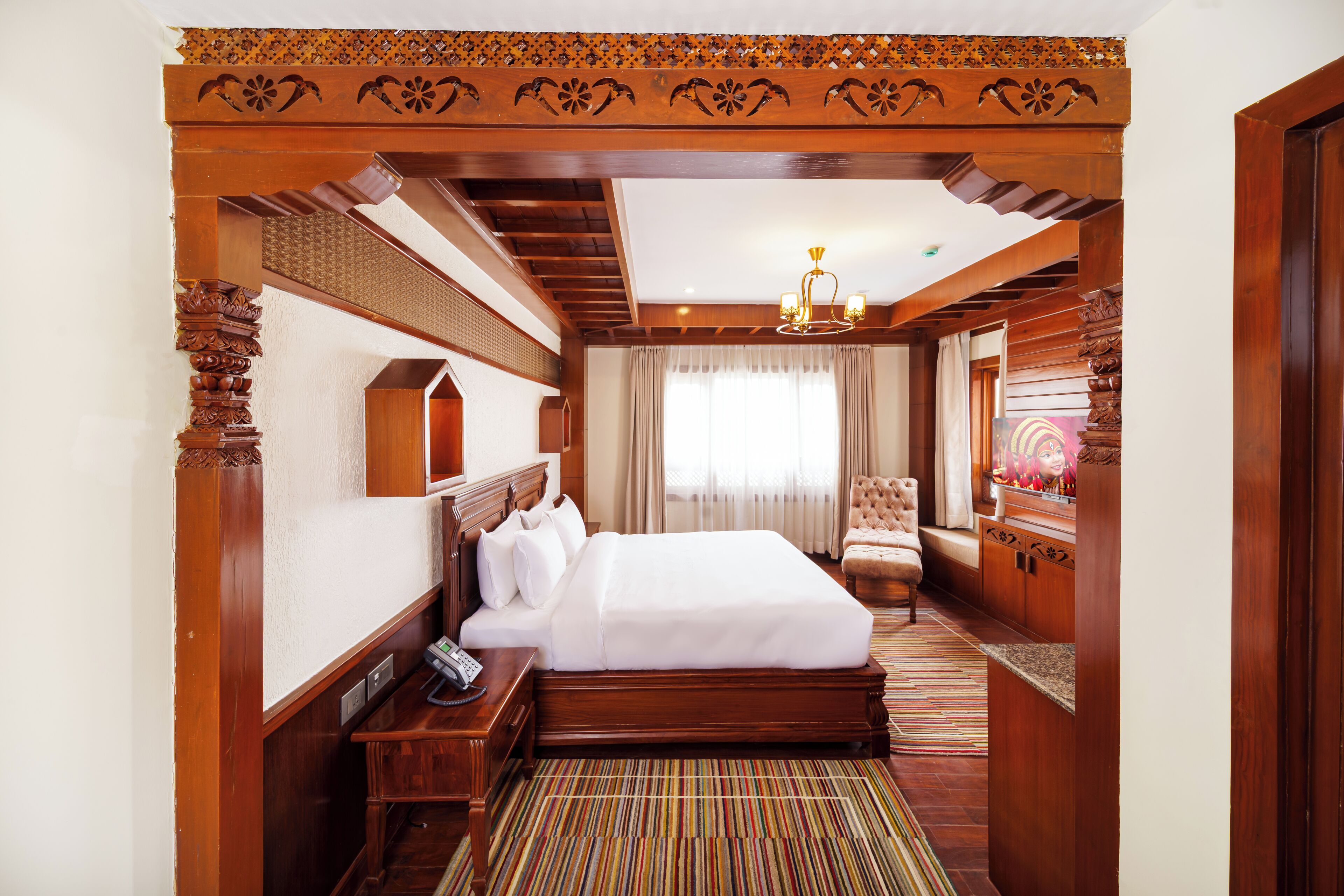 Habitación de hotel con una cama grande, cabecera de madera, un escritorio pequeño con un teléfono, una silla y un espejo.