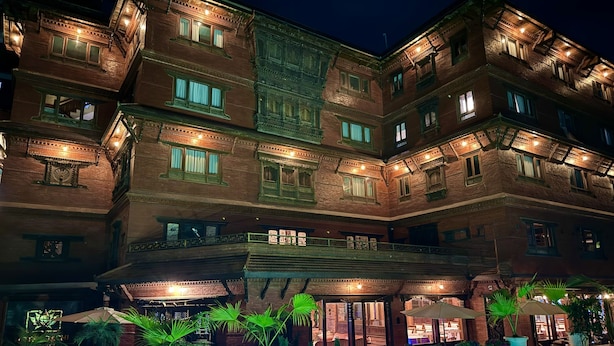 Un hotel de varios pisos con zona de piscina, mobiliario exterior y plantas en macetas.