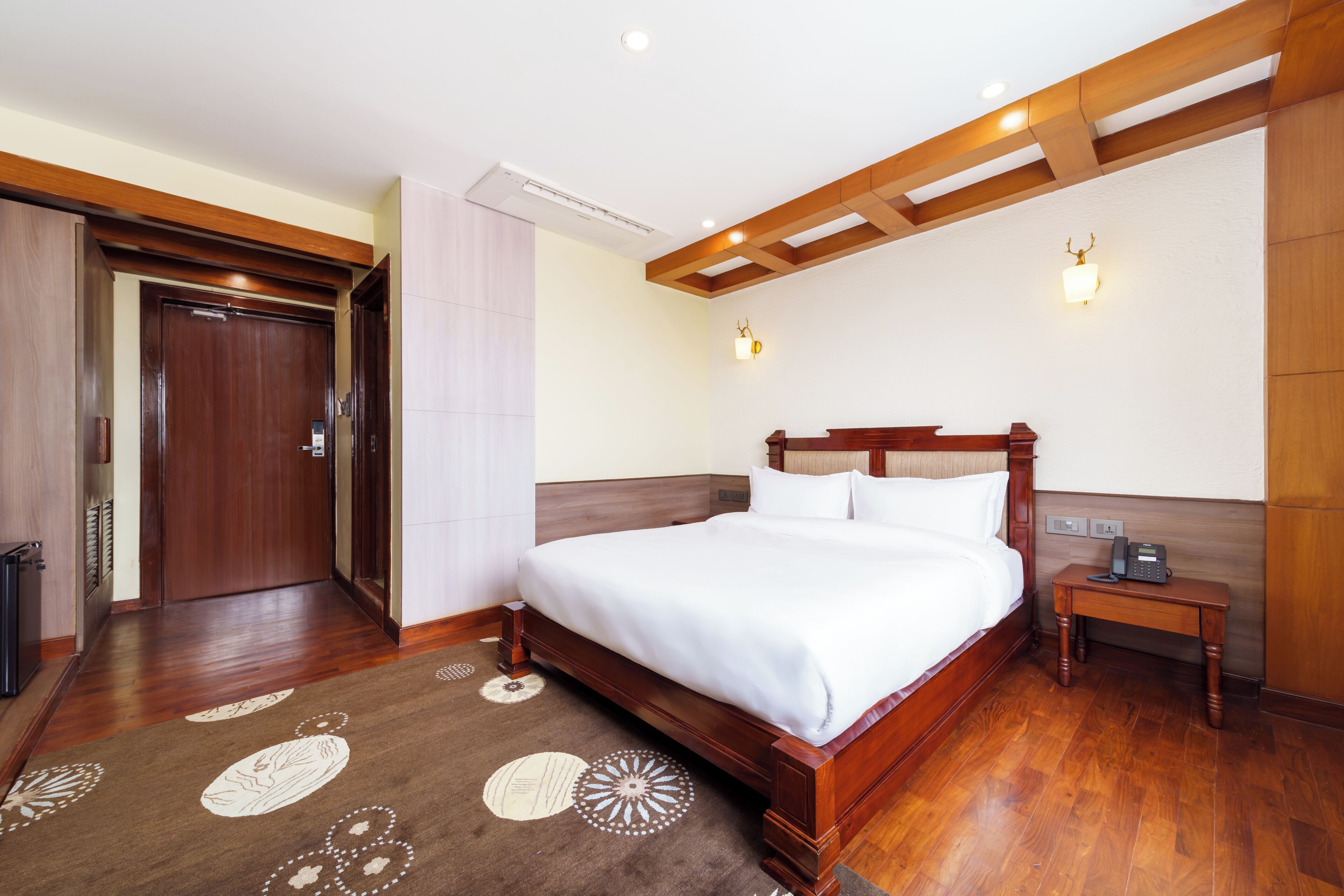 Ein Hotelzimmer mit einem hölzernen Bett, einem Nachttisch, einer Wandleuchte und einer Tür.