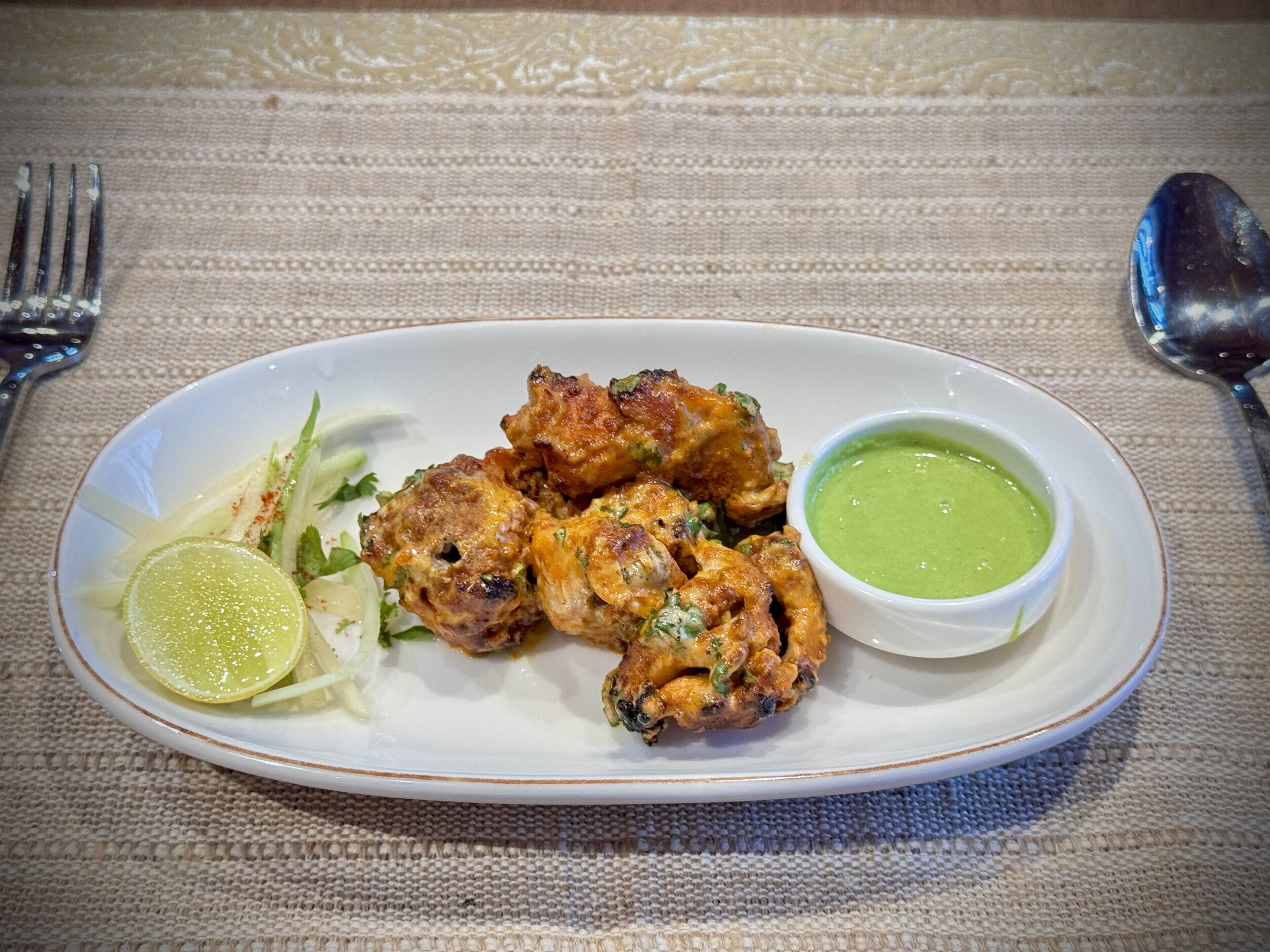 A plate of food with a lime wedge and green sauce, on a textured tablecloth.