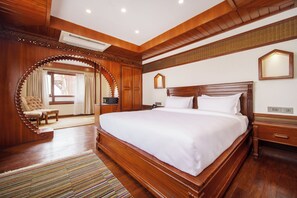 Une chambre spacieuse avec un grand lit, un plancher en bois, un grand miroir rond et une armoire intégrée.