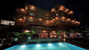 Un hotel de varios pisos con piscina, mobiliario exterior y plantas en macetas.