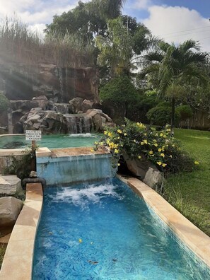 A swimming pool with a waterfall feature, surrounded by greenery and a warning sign. - Mwembe Resort Malindi (Malindi)