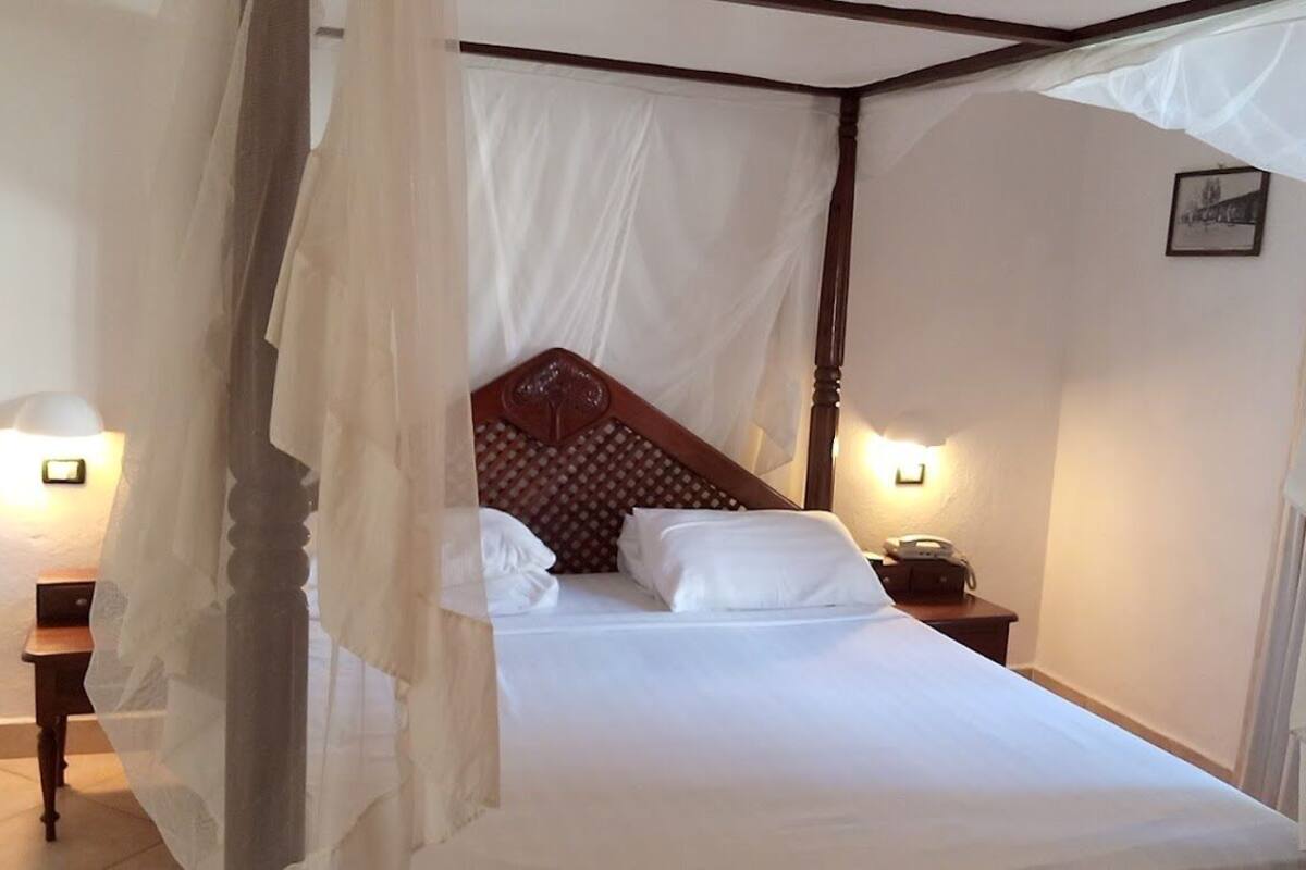 A bedroom with a canopy bed, bedside lamps, and a nightstand with a telephone.