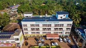 Un immeuble à plusieurs étages, doté de panneaux solaires sur le toit, un parking avec plusieurs voitures et un panneau indiquant un restaurant appelé « Pandurang ».