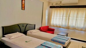 Une chambre d’hôtel avec deux lits, une chaise rouge, une petite table et une fenêtre avec des rideaux.