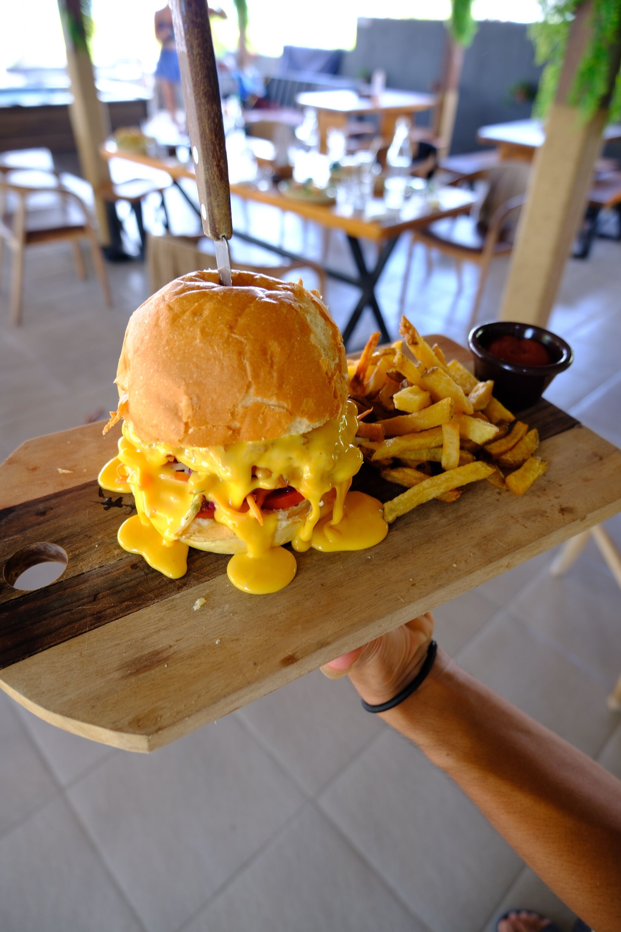 A wooden serving board with a burger and fries, held by a person.