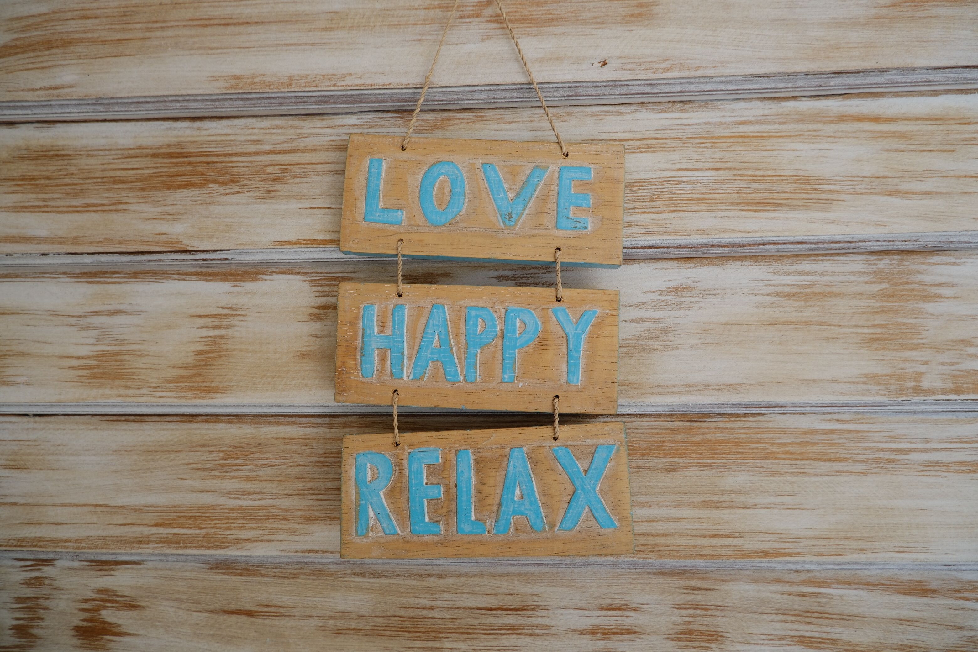 A wooden sign with the words 'LOVE,' 'HAPPY,' and 'RELAX' hanging on a wooden wall.