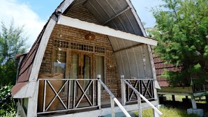 Uma cabana de madeira com telhado inclinado, varanda com grades e janela com padrão quadriculado.