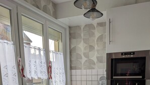 Een moderne keuken met een roestvrijstalen spoelbak, witte kasten, een ingebouwde oven en een raam met gordijnen.