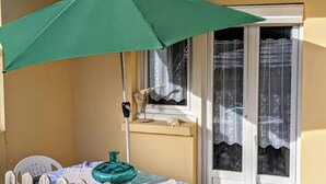 Een klein balkon met een tafel, een stoel en een groene parasol.