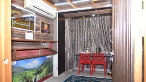Una habitación con una televisión de pantalla plana grande, una silla roja, una cortina estampada y una pequeña mesa con un hervidor.