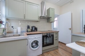 A compact kitchen with a washing machine, a coffee maker, and a built-in oven. - Modern Studio With Free Parking And Garden (Greater London)