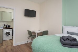 A hotel room with a bed, a desk, a chair, a washing machine, and a flat-screen TV. - Modern Studio With Free Parking And Garden (Greater London)