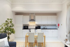 A modern kitchen with white cabinets, a black countertop, and a dining area with a table and chairs. - Hertford Flat 3 (London)