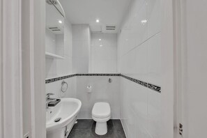 A small, white bathroom with a toilet, sink, and shower. - Hertford Flat 4 (London)