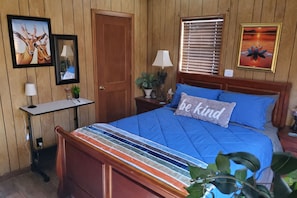 Une chambre à coucher avec un lit en bois, un bureau, une chaise, une porte et deux tableaux encadrés accrochés au mur.