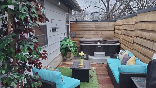 Eine Terrassenanlage mit einer schwarzen Outdoor-Sofaecke, einem kleinen Tisch mit einer Vase und einem Whirlpool.