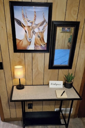 Un espace de travail comprenant un bureau, une lampe, une plante et des œuvres d’art encadrées sur un mur en bois.