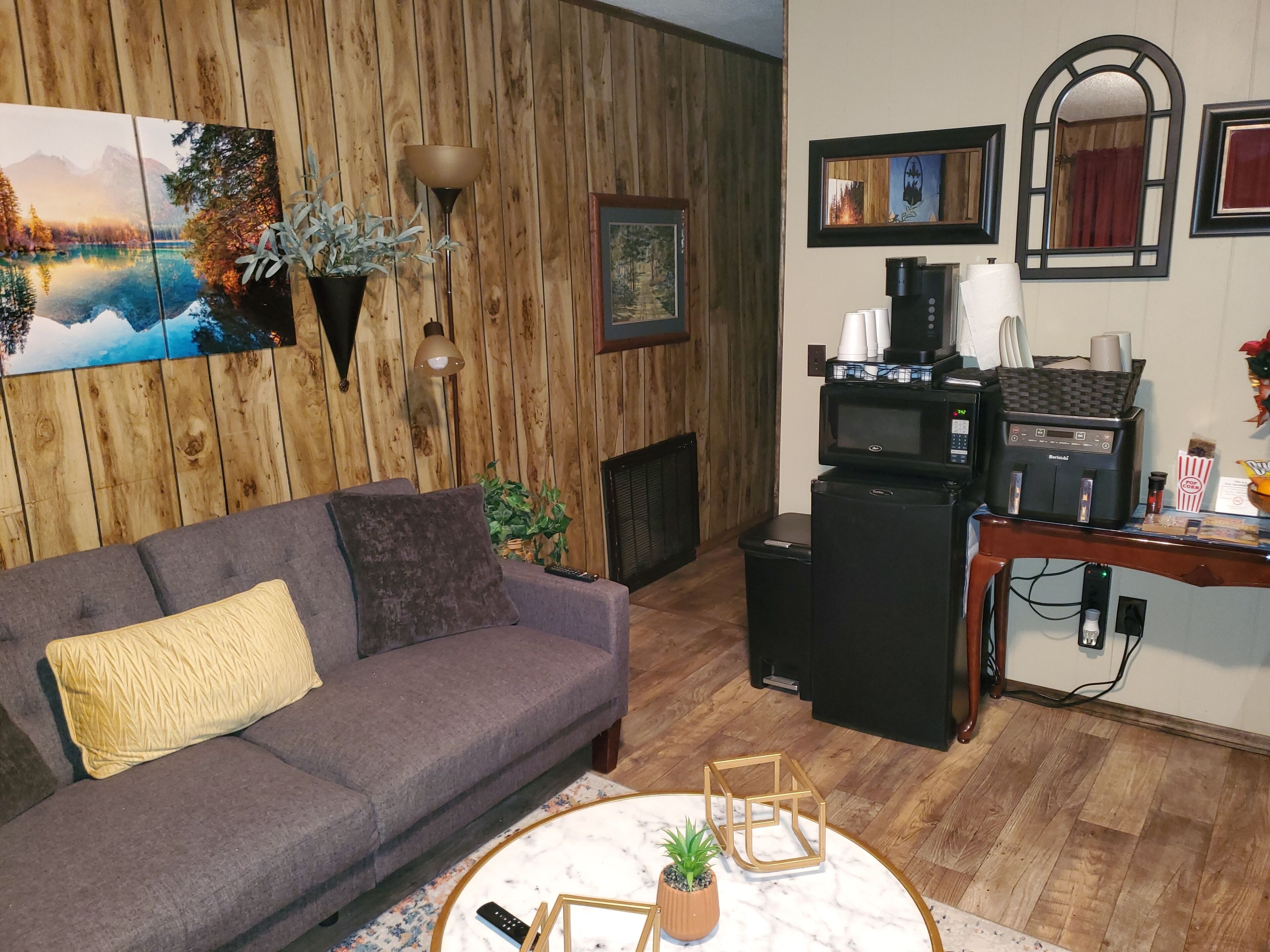 A living room with a gray sofa, a coffee machine, and a TV on a wooden wall.