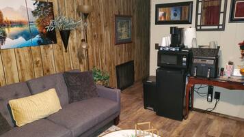 A living room with a gray sofa, a coffee machine, and a TV on a wooden wall.