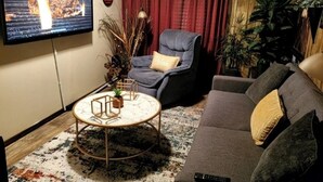 Ein Wohnzimmer mit Flachbildfernseher, grauem Sofa, blauem Sessel, rundem Couchtisch und rotem Vorhang.