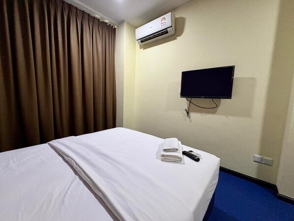 A hotel room with a bed, an air conditioner, a TV, and a remote control on the bed. - OYO 91290 Cozitel (Bintulu)