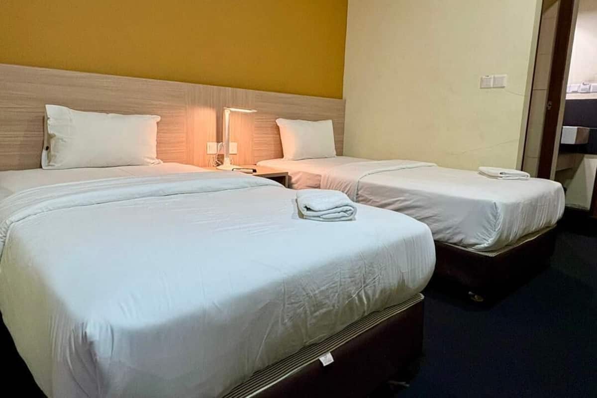 Two single beds with white linens, a wooden headboard, bedside lamps, and a plain wall.