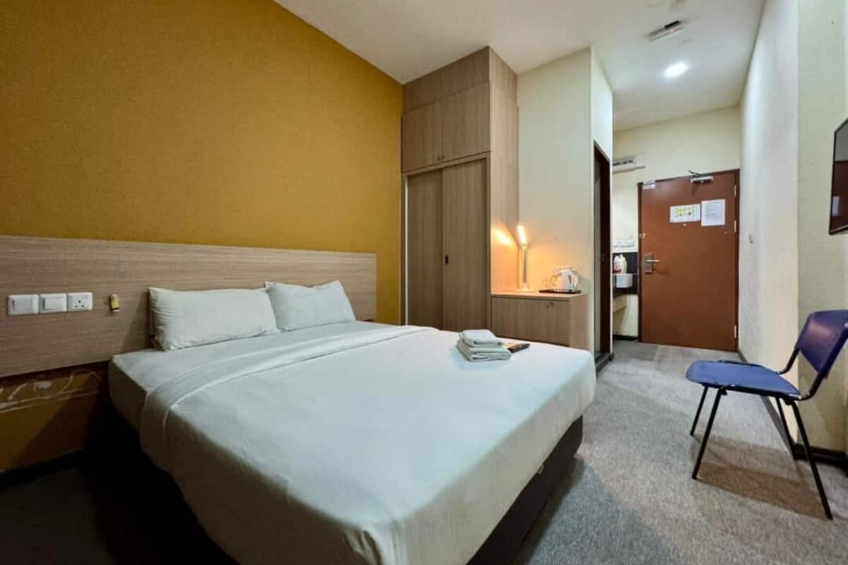 A hotel room with a large bed, a wooden wardrobe, a desk with a lamp, and a chair.
