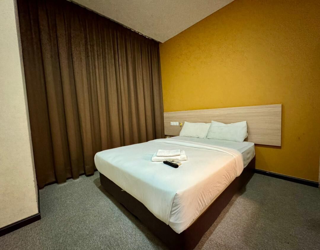 Una habitación de hotel con una cama, cortinas y una pared amarilla.